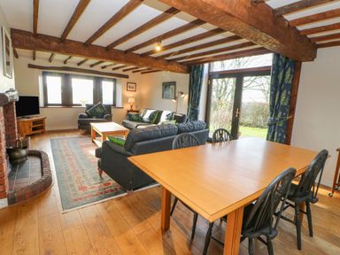 A living room with wooden beams on the ceiling a wooden dining table with black chairs sofas and a brick fireplace at Hadrian's View Banks near Brampton