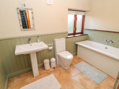 A bathroom with a sink toilet bathtub window and rugs at Hadrian's View Banks near Brampton