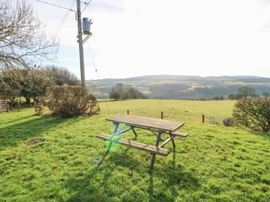 A wooden picnic table on grass with hills and trees in the background at Hadrian's View in Banks near Brampton