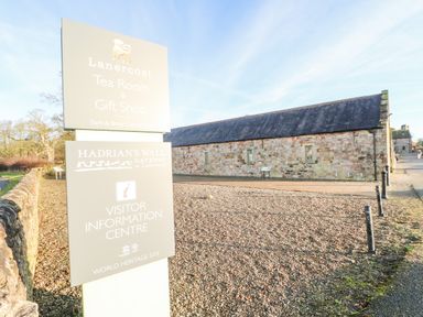 An outdoor view of a visitor information centre with a stone building and signposts at Hadrian's View in Banks near Brampton