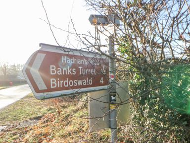 A road sign pointing to Banks Turret and Birdoswald along a country road near bushes at Hadrians View Banks near Brampton