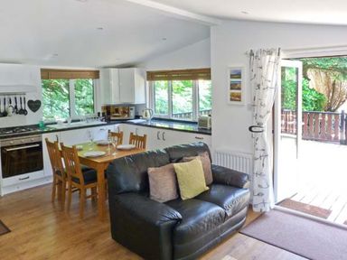 A living area with a black leather sofa and wooden dining table near an open door to a balcony at Top Lodge 4 Skiptory Howe White Cross Bay near Troutbeck Bridge
