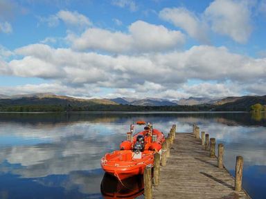 A wooden dock extending into a lake with an orange boat tied to it and hills in the background at Top Lodge 4 Skiptory Howe White Cross Bay near Troutbeck Bridge