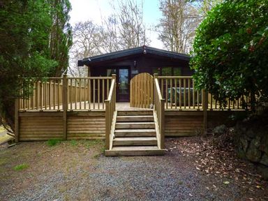 A wooden cabin with a raised deck and stairs surrounded by trees at Top Lodge 4 Skiptory Howe White Cross Bay near Troutbeck Bridge