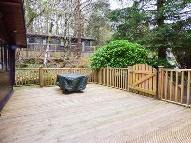 A wooden outdoor deck with a covered table surrounded by a wooden fence and gate at Top Lodge 4 Skiptory Howe White Cross Bay near Troutbeck Bridge