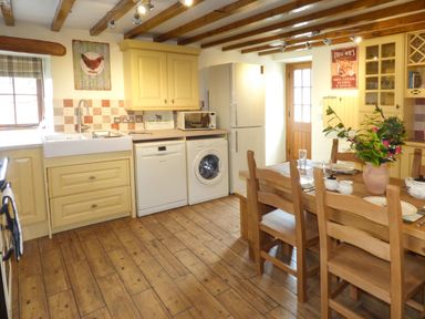 A kitchen with yellow cabinets wooden dining table and chairs and appliances at Fell View Cottage in Bootle near Millom