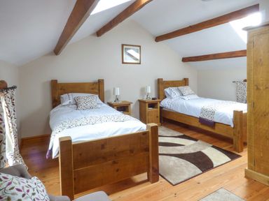 A bedroom with two wooden beds bedside tables lamps armchair and a rug at Fell View Cottage in Bootle near Millom