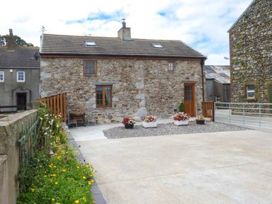 Exterior stone cottage with wooden door and windows surrounded by flower pots and a gravel area at Fell View Cottage in Bootle near Millom