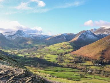 A valley with green fields and scattered houses surrounded by snow capped mountains