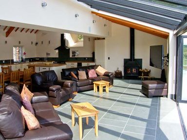 A living area with brown leather sofas wooden tables wood burning stove and dining table at Garth Morthin The Barn in Porthmadog