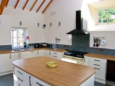 A kitchen with wooden countertops white cabinets a central island a stove and range hood at Garth Morthin The Barn in Porthmadog