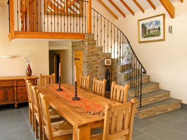 A dining room with a wooden table and chairs a staircase with stone steps and black railing at Garth Morthin The Barn in Porthmadog