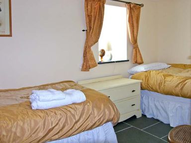 A bedroom with two single beds a chest of drawers and a window with curtains at Garth Morthin The Barn in Porthmadog