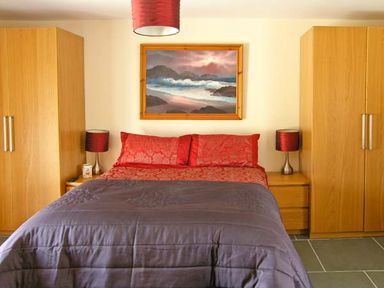 A bedroom with a bed with red pillows and sheets and a gray comforter flanked by wooden wardrobes and bedside tables at Garth Morthin The Barn in Porthmadog