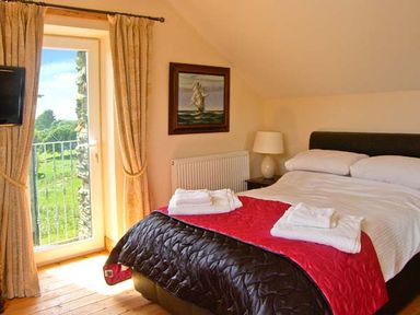 A bedroom with a double bed bedside table lamp painting on the wall and door leading outside at Garth Morthin The Barn in Porthmadog