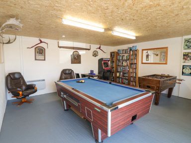 A game room with a pool table foosball table arcade machine bookshelves and chairs at Garth Morthin The Stables in Porthmadog