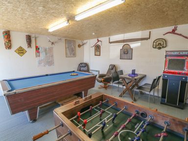 A game room with a pool table foosball table arcade machine chairs and a small table at Garth Morthin The Stables in Porthmadog