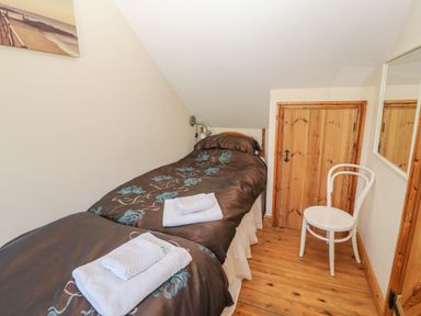 A small bedroom with two single beds a white chair a wooden floor and a small wooden door at Garth Morthin The Stables in Porthmadog