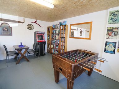 A game room with foosball table arcade machine bookshelf and a table with chairs at Garth Morthin The Stables in Porthmadog