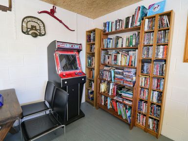 A room with bookshelves filled with books and DVDs an arcade game and two black chairs at Garth Morthin The Stables in Porthmadog