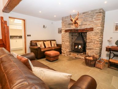 A living room with brown leather sofas a stone fireplace with a wood burner and a doorway leading to a kitchen at Garth Morthin The Stables in Porthmadog
