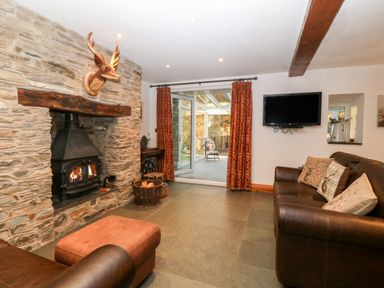A living room with a stone fireplace a mounted deer head and brown leather sofas at Garth Morthin The Stables in Porthmadog