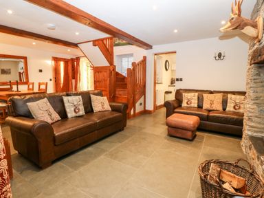 A living room with two leather sofas wooden staircase and a stone fireplace at Garth Morthin The Stables in Porthmadog