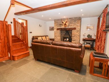 A living room with brown leather sofas a stone fireplace wooden stairs and red patterned curtains at Garth Morthin The Stables in Porthmadog