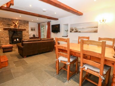 A living room with a wooden dining table and chairs and a stone fireplace with a mounted stag head at Garth Morthin The Stables in Porthmadog
