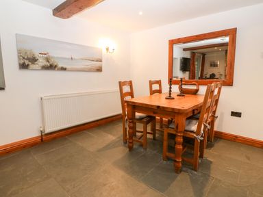 A dining area with a wooden table and chairs a large wall mirror and a landscape painting at Garth Morthin The Stables in Porthmadog