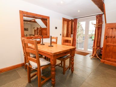 A dining area with a wooden table and four chairs next to glass doors with red curtains at Garth Morthin The Stables in Porthmadog