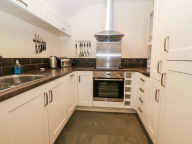A kitchen with white cabinets stainless steel oven and hood a toaster kettle and hanging utensils at Garth Morthin The Stables in Porthmadog