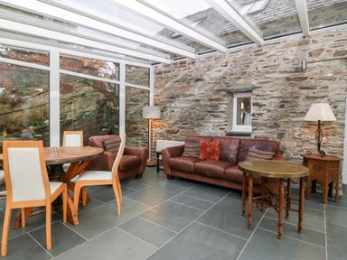 A room with leather sofa and chair a round dining table with wooden chairs and a stone wall at Garth Morthin The Stables in Porthmadog