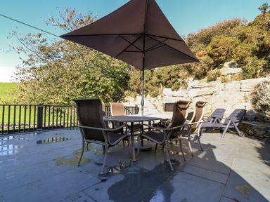 An outdoor patio area with a table and chairs under a large umbrella and two lounge chairs at Garth Morthin The Stables Porthmadog