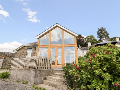 A stone house with large glass windows and wooden frames stairs and bushes outside at Llety'r Wennol Ffarmers near Lampeter