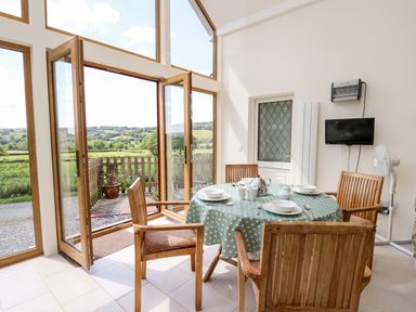 A dining area with wooden chairs and a table with a polka dot tablecloth near large glass doors at Llety'r Wennol in Ffarmers near Lampeter