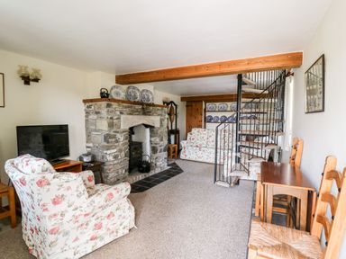 A living room with floral armchairs stone fireplace spiral staircase and wooden chairs at Llety'r Wennol Ffarmers near Lampeter