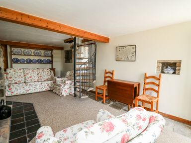 A living room with floral sofas a spiral staircase wooden chairs and a folding table with plates on a shelf at Llety'r Wennol Ffarmers near Lampeter