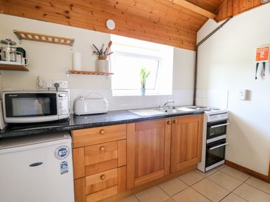 A kitchen with wooden cabinets a microwave toaster mini fridge stove and a plant on the windowsill at Llety'r Wennol Ffarmers near Lampeter