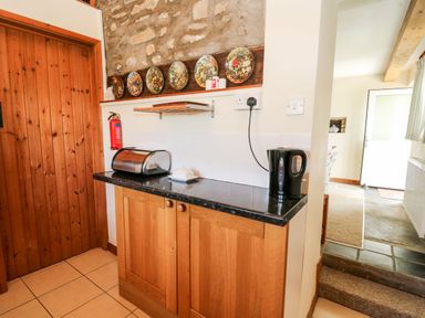 A kitchen counter with a bread box and electric kettle next to a wooden door at Llety'r Wennol Ffarmers near Lampeter