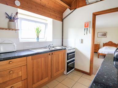 A kitchen with wooden cabinets a sink a stove and utensils near a bedroom at Llety'r Wennol in Ffarmers near Lampeter
