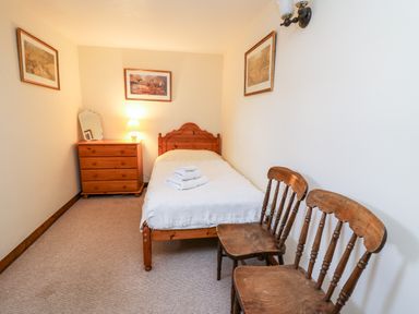 A small bedroom with a single bed, wooden dresser, two wooden chairs, and framed pictures on the walls at Llety'r Wennol in Ffarmers near Lampeter