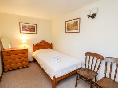 A small bedroom with a wooden bed and dresser a lamp folded towels and two wooden chairs on the side at Llety'r Wennol Ffarmers near Lampeter