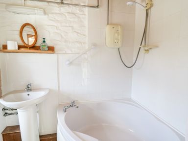 A bathroom with a corner bathtub a shower head and a pedestal sink at Llety'r Wennol in Ffarmers near Lampeter
