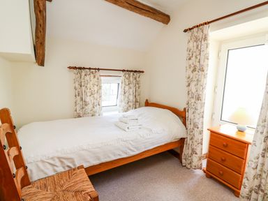 A small bedroom with a single bed a wooden chair a wooden chest of drawers and floral curtains at Llety'r Wennol Ffarmers near Lampeter