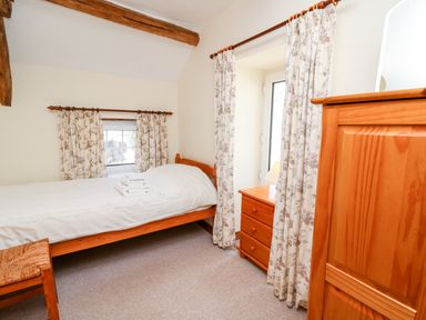 A bedroom with a single bed wooden furniture and floral curtains at Llety'r Wennol Ffarmers near Lampeter