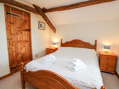 A bedroom with a wooden bed frame and bedside tables with lamps at Llety'r Wennol in Ffarmers near Lampeter