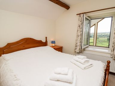A bedroom with a wooden bed and folded towels on the white bedspread next to an open window with floral curtains at Llety'r Wennol in Ffarmers near Lampeter