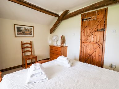 A bedroom with a wooden chair a wooden dresser with a fan and mirror a wooden door and a bed with folded towels at Llety'r Wennol Ffarmers near Lampeter