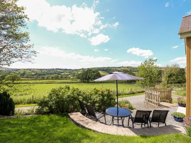 An outdoor patio area with table chairs and umbrella overlooking green fields and hills at Llety'r Wennol in Ffarmers near Lampeter